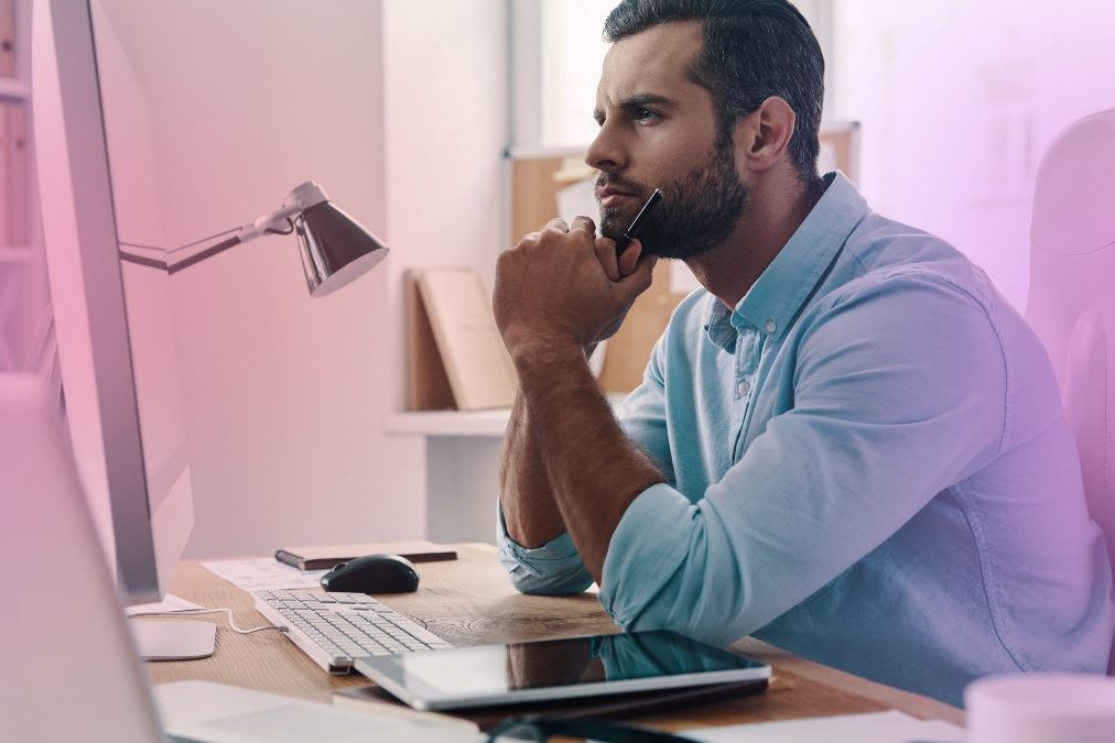 An office worker at a desk, pausing between screens and paperwork