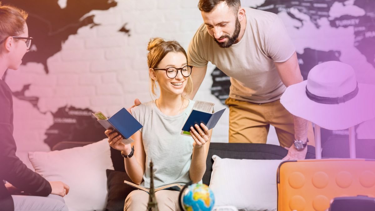 A couple reading their passports in front of a world map with luggage packed