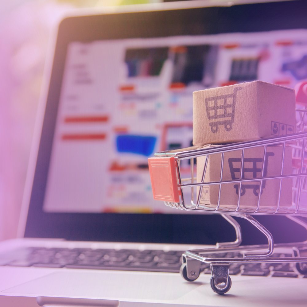 A miniature shopping cart of parcels in front of an online store on a laptop